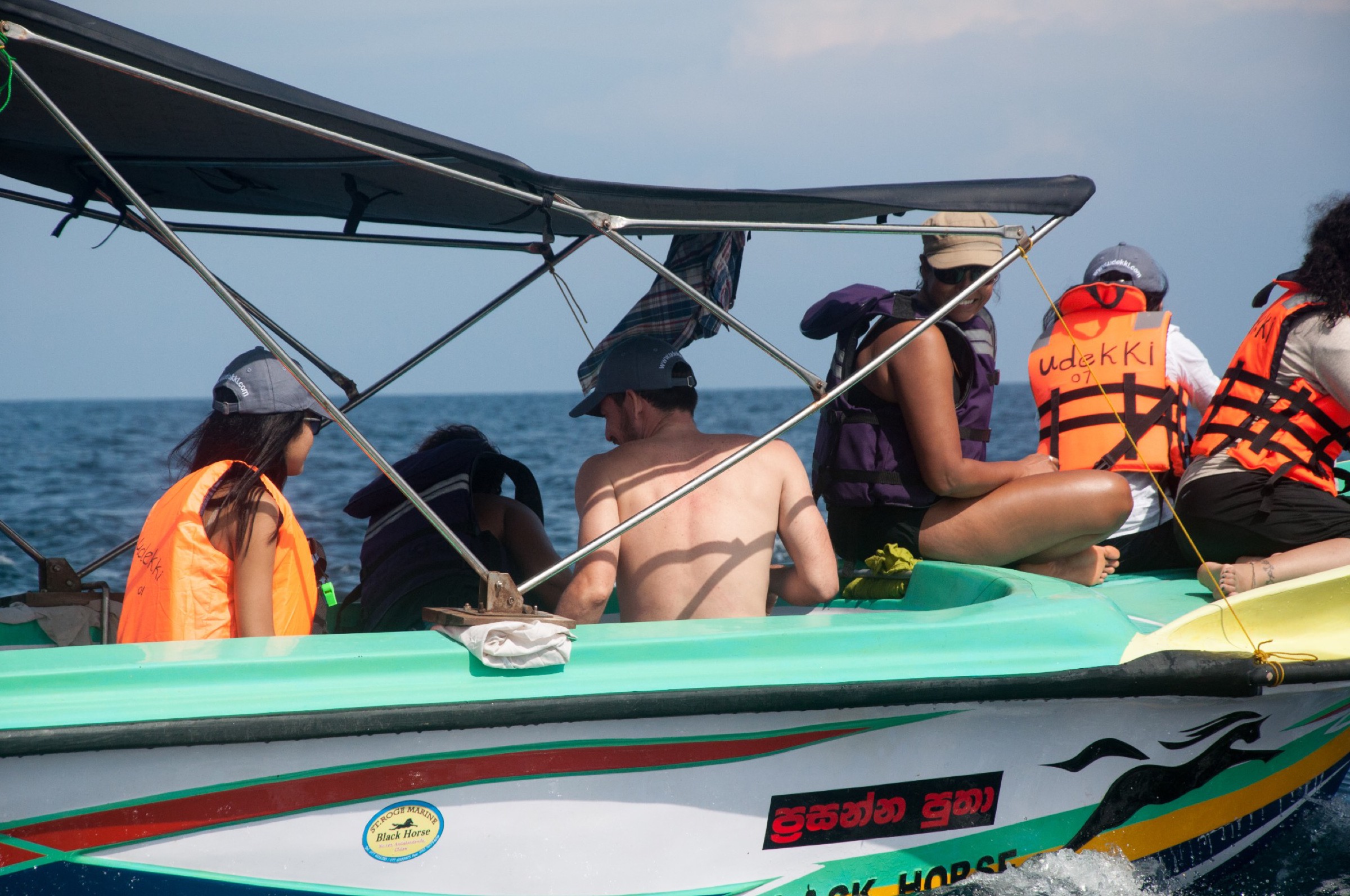 Passengers in orange life jackets sitting on a small boat at sea.